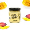 Słoik miodu z serii cud z mango 250g firmy Sądecki Bartnik. Słoik leży w otoczeniu mango. Etykieta na słoiku ma napis: "Cud miód i mango" oraz informacjami o produkcie. Zakrętka jest w kolorze czarnym.