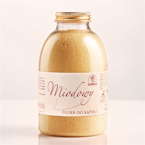Miodowy puder do kąpieli o gramaturze 400g. Zdjęcie przedstawia plastikową butelkę z beżową etykietą, na której są niezbędne informacje o produkcie oraz złotą zakrętką. Puder jest w kolorze żółtym.