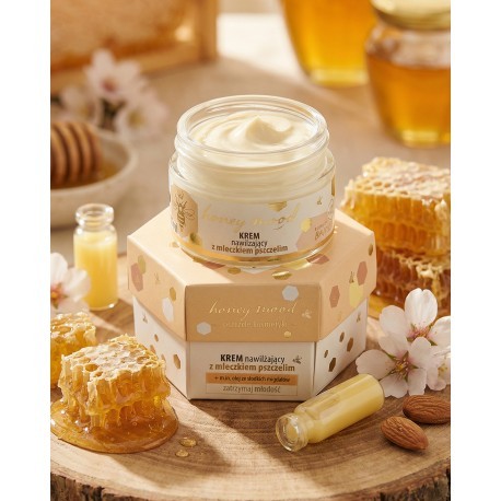Krem nawilżający Honey Mood o pojemności 50ml, który stoi na podniesieniu, czyli pudełku w które jest zapakowany słoiczek z kremem. Pudełko ma heksagonalny kształt. W otoczeniu są ampułki z mleczkiem pszczelim oraz plastry miodu z białymi kwiatami.